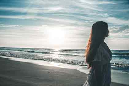 A photo of a woman standing by the seashore, looking out at the sea