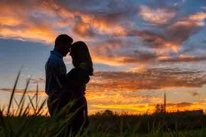 A photo of a couple passionately looking at each other with the sunset behind them