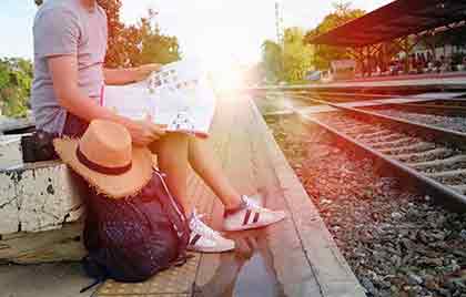 A photo of a man sitting beside a train track while looking at a map